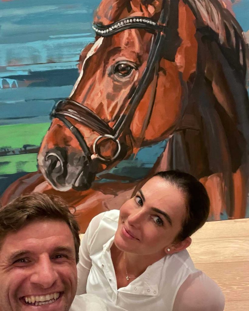 der Fußballstar Thomas Müller und seine Frau Lisa vor einem Porträt ihres Pferdes D'avie von Hartmut Hellner